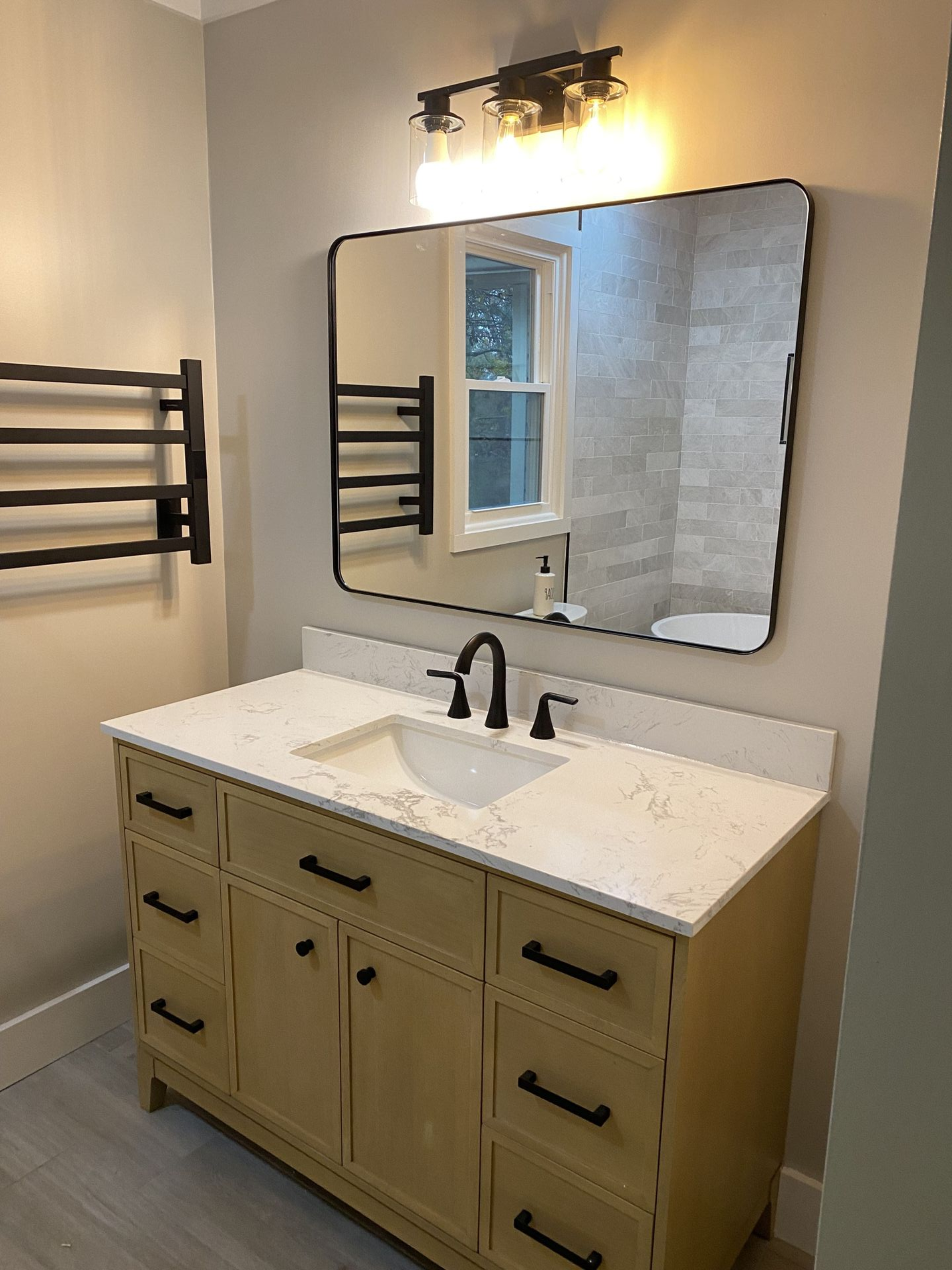 Bathroom vanity with a black-framed mirror, light fixture, and black fixtures. Includes a towel warmer.