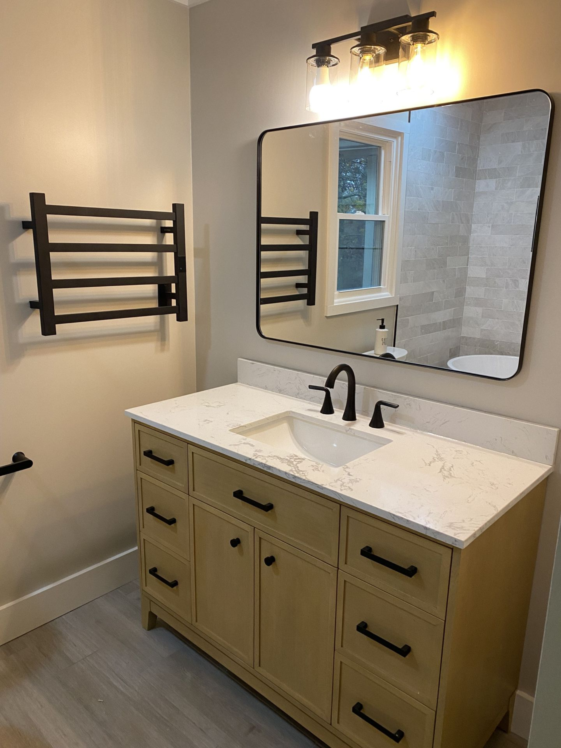 Bathroom with light beige vanity, black fixtures, heated towel rack, and large mirror.
