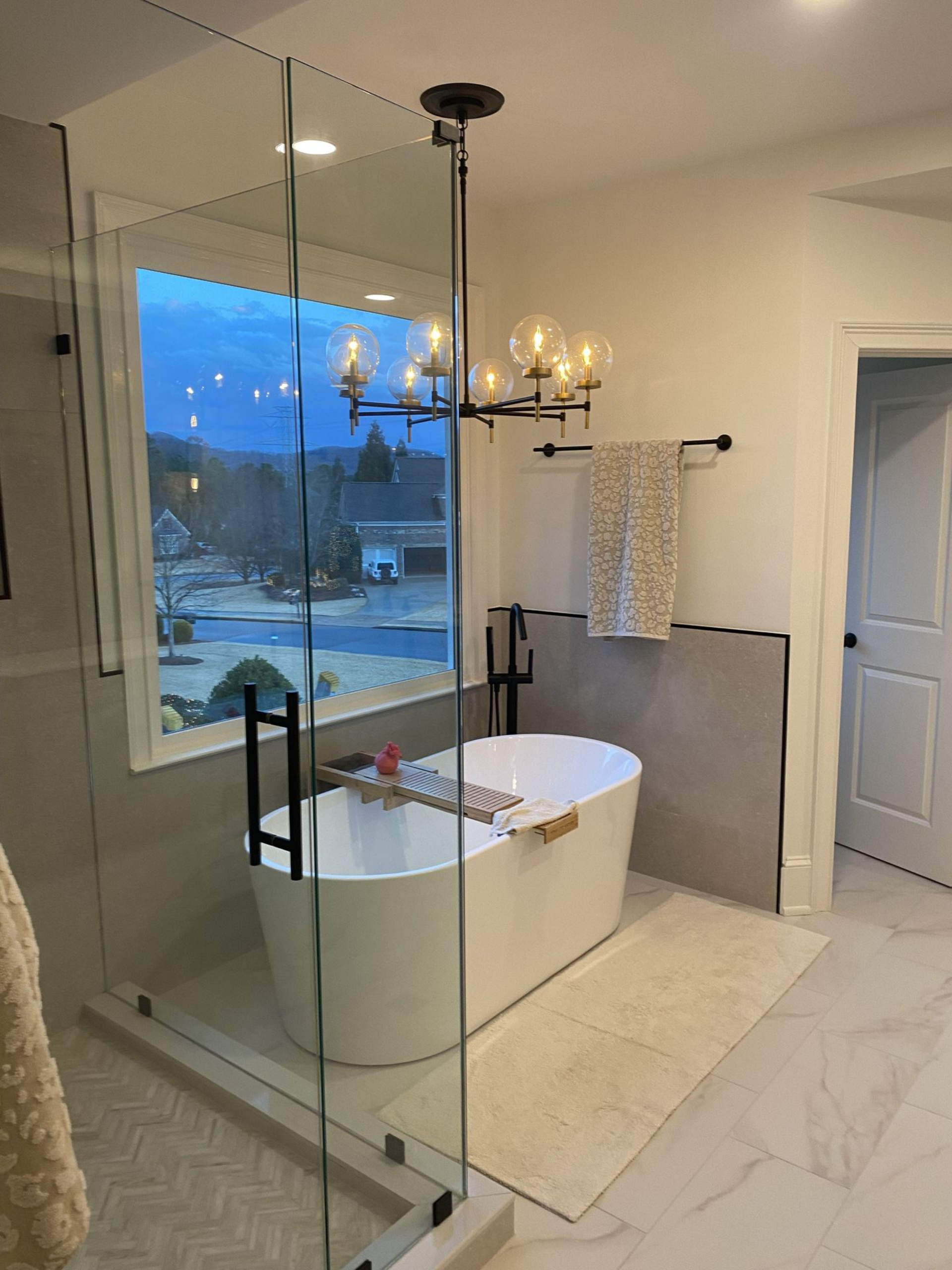 Modern bathroom with a freestanding tub, glass shower, and large window overlooking a residential area.