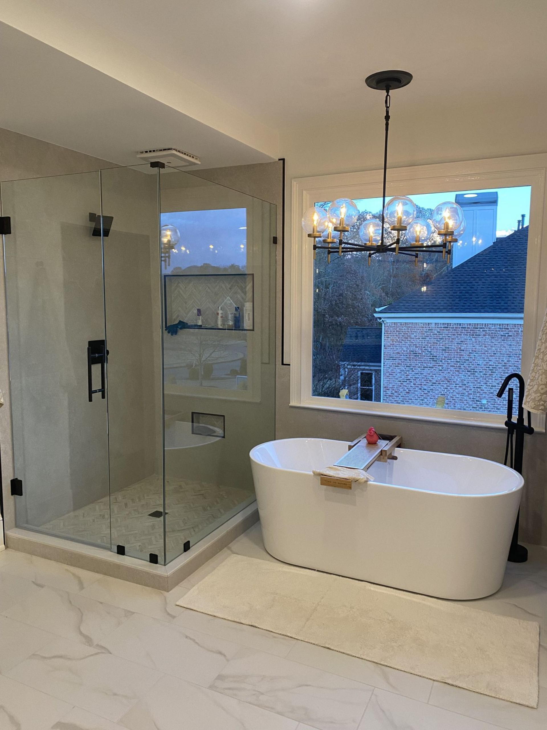 Modern bathroom with glass shower, freestanding tub, and a window overlooking a neighborhood.