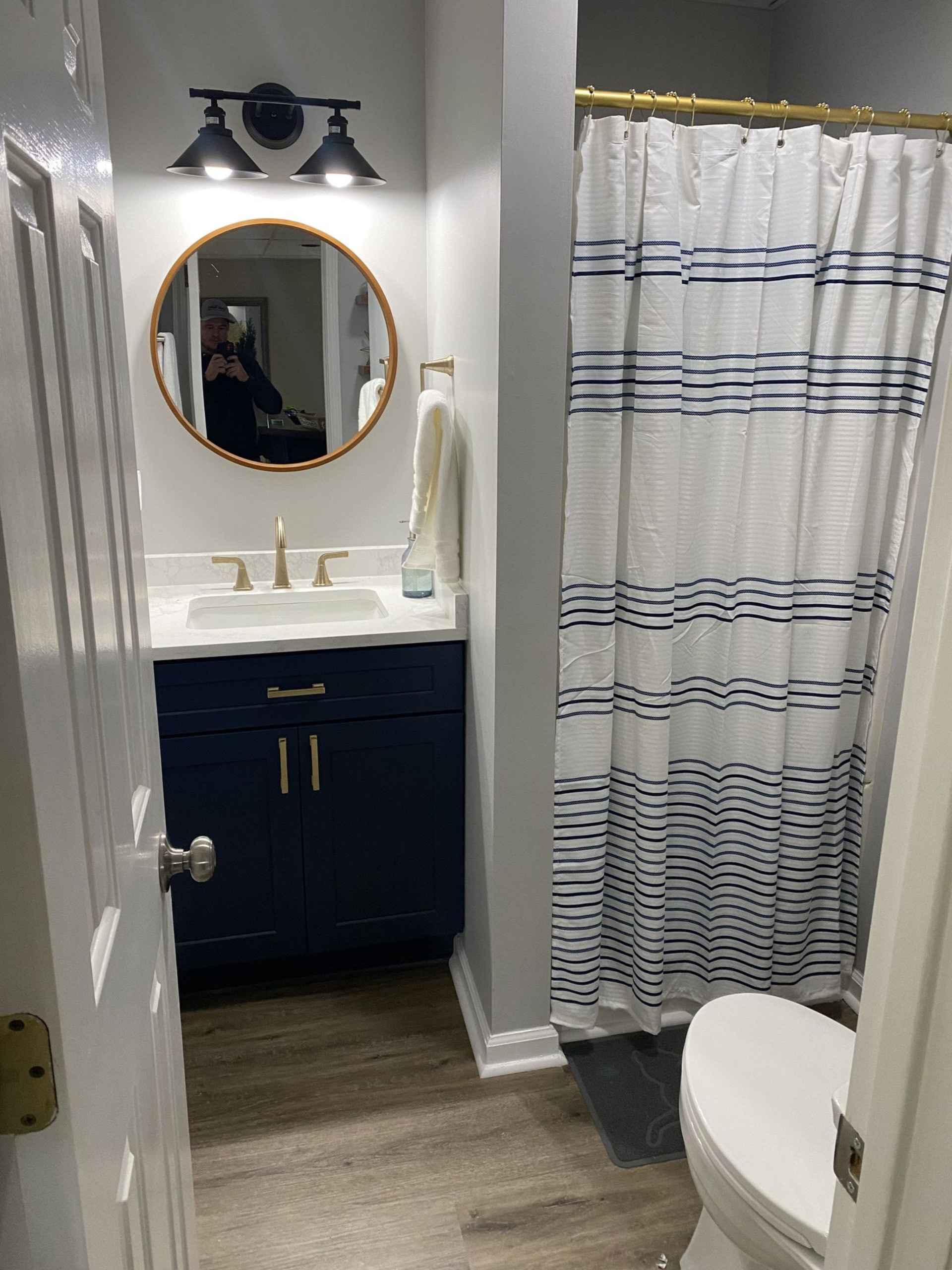 Small bathroom with navy vanity, round mirror, and striped shower curtain.