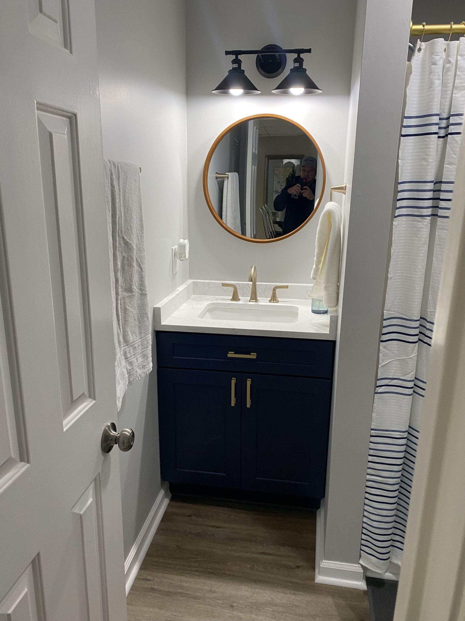 Small bathroom with a navy blue vanity, round mirror, and striped shower curtain.