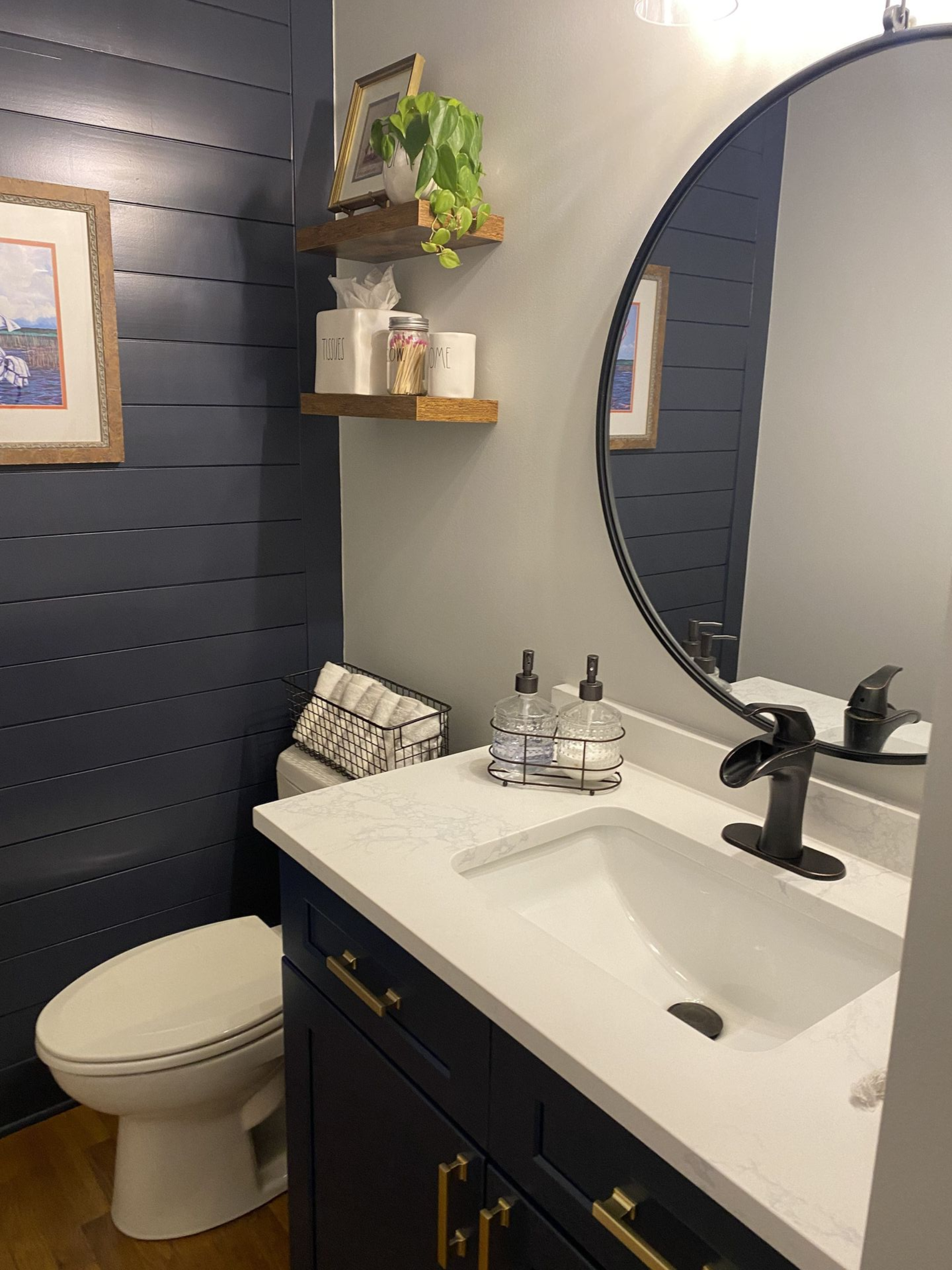 Navy blue and white bathroom with a toilet, sink, mirror, and shelves with decorations.