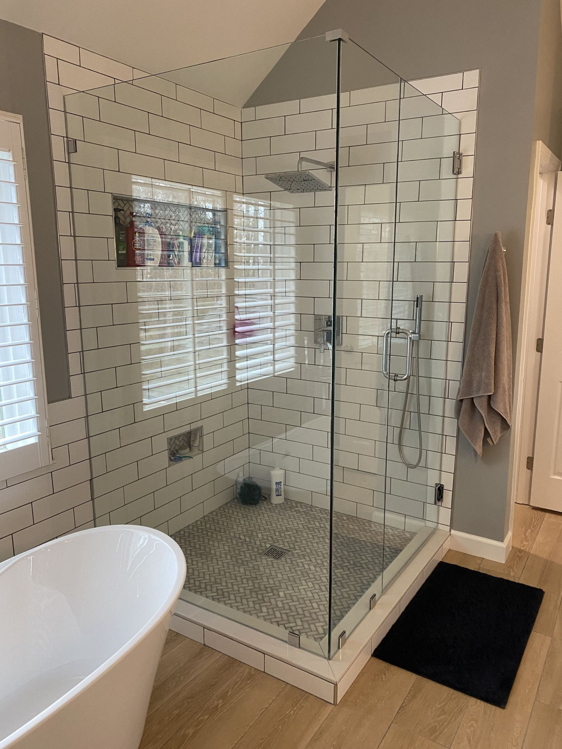 Modern bathroom with glass shower, white tile, and a standalone tub.