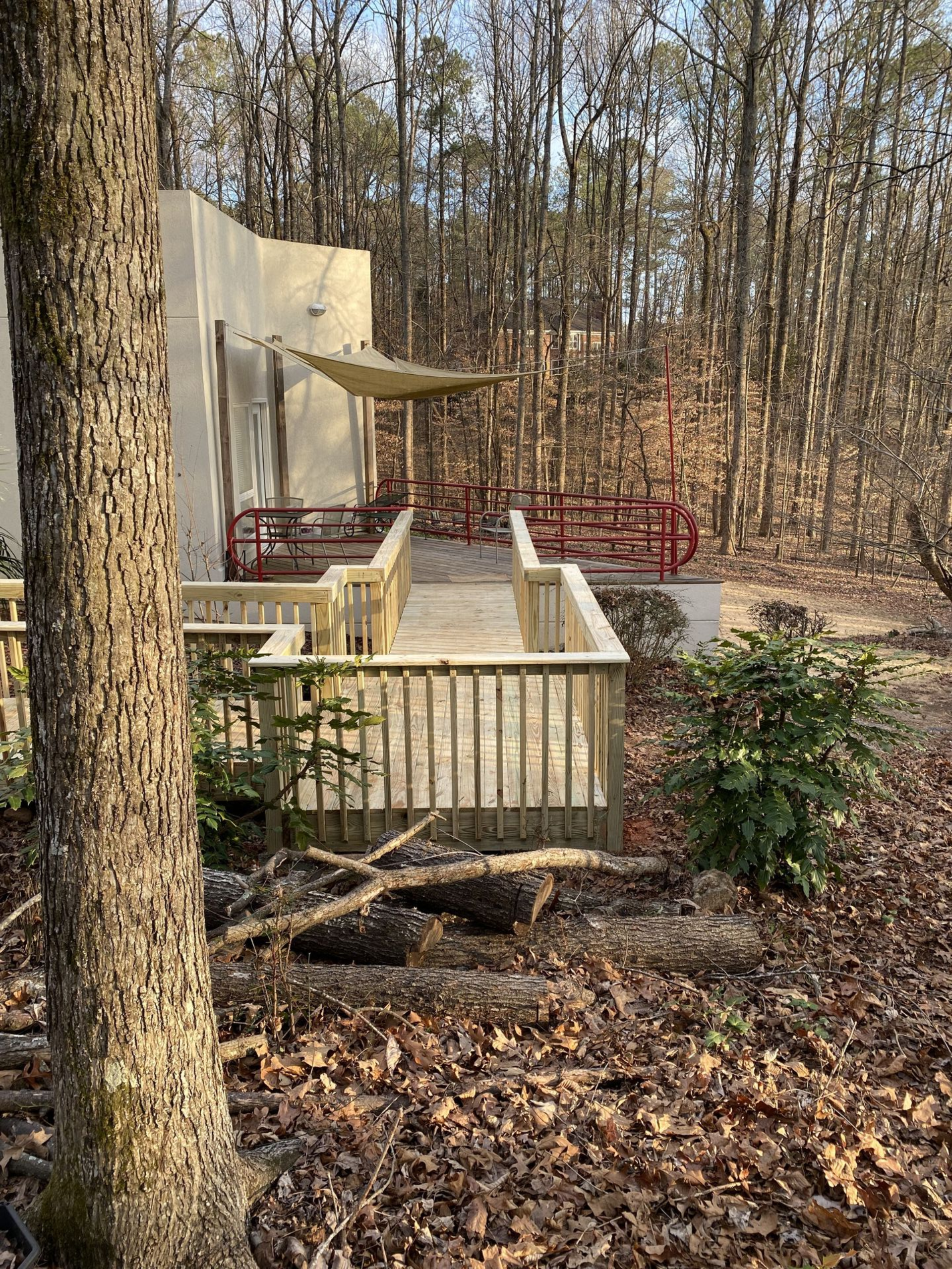Wooden deck with a building in a wooded area; tan awning, red railings.