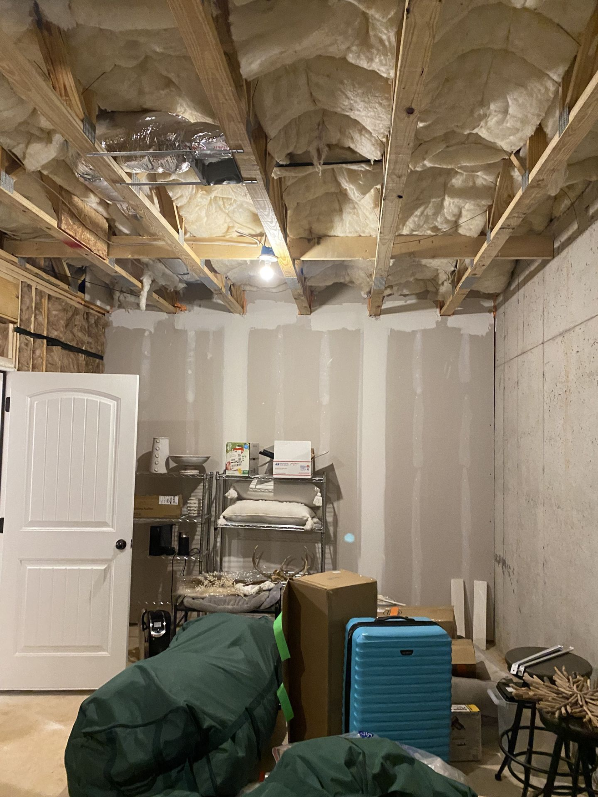 Unfinished basement with exposed ceiling beams and drywall, cluttered with boxes and a suitcase.