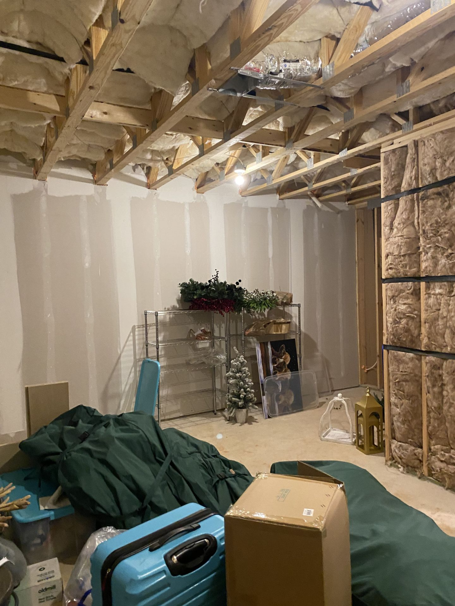 Unfinished basement with exposed ceiling beams and insulation, drywall, and clutter.