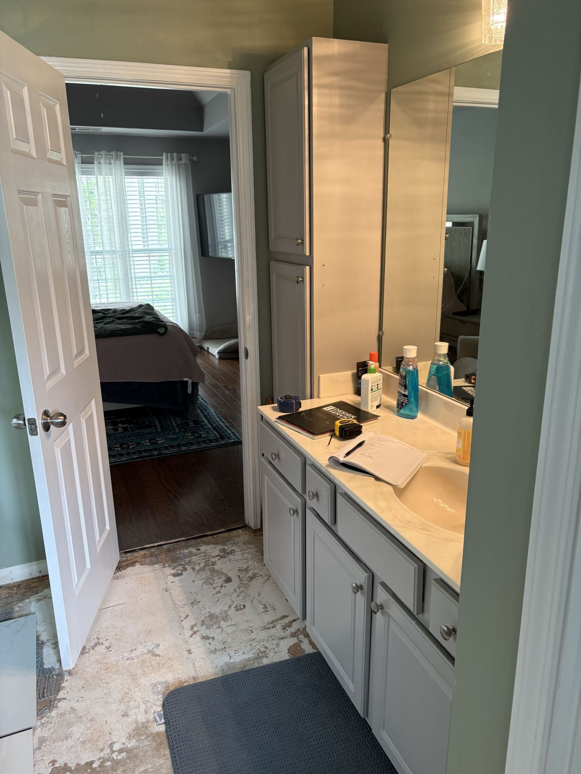 Bathroom interior with vanity, storage cabinet, open doorway to bedroom, and floor damage.