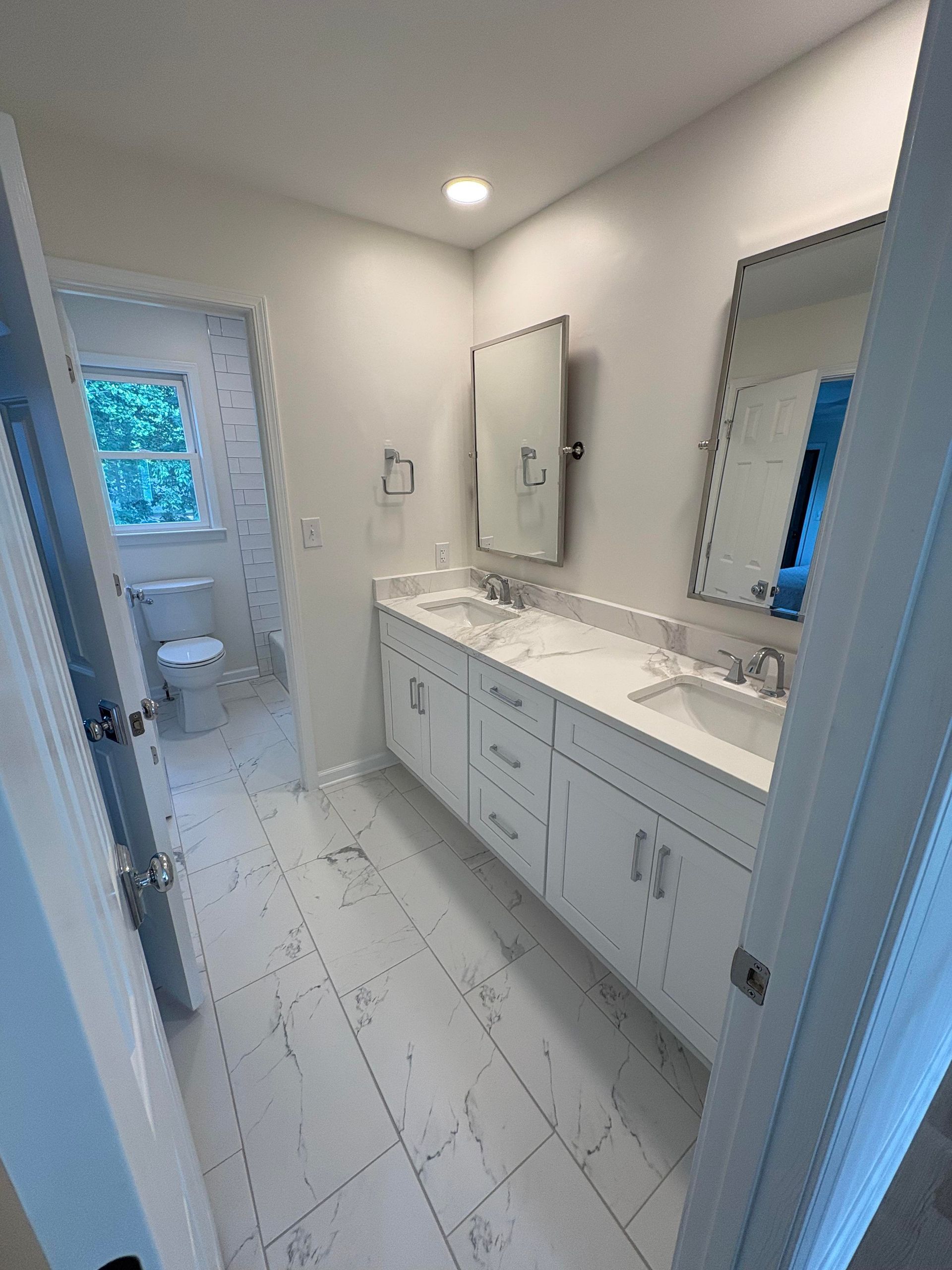Bathroom with white vanity, marble-look floor, and dual sinks. A toilet is visible in the background.