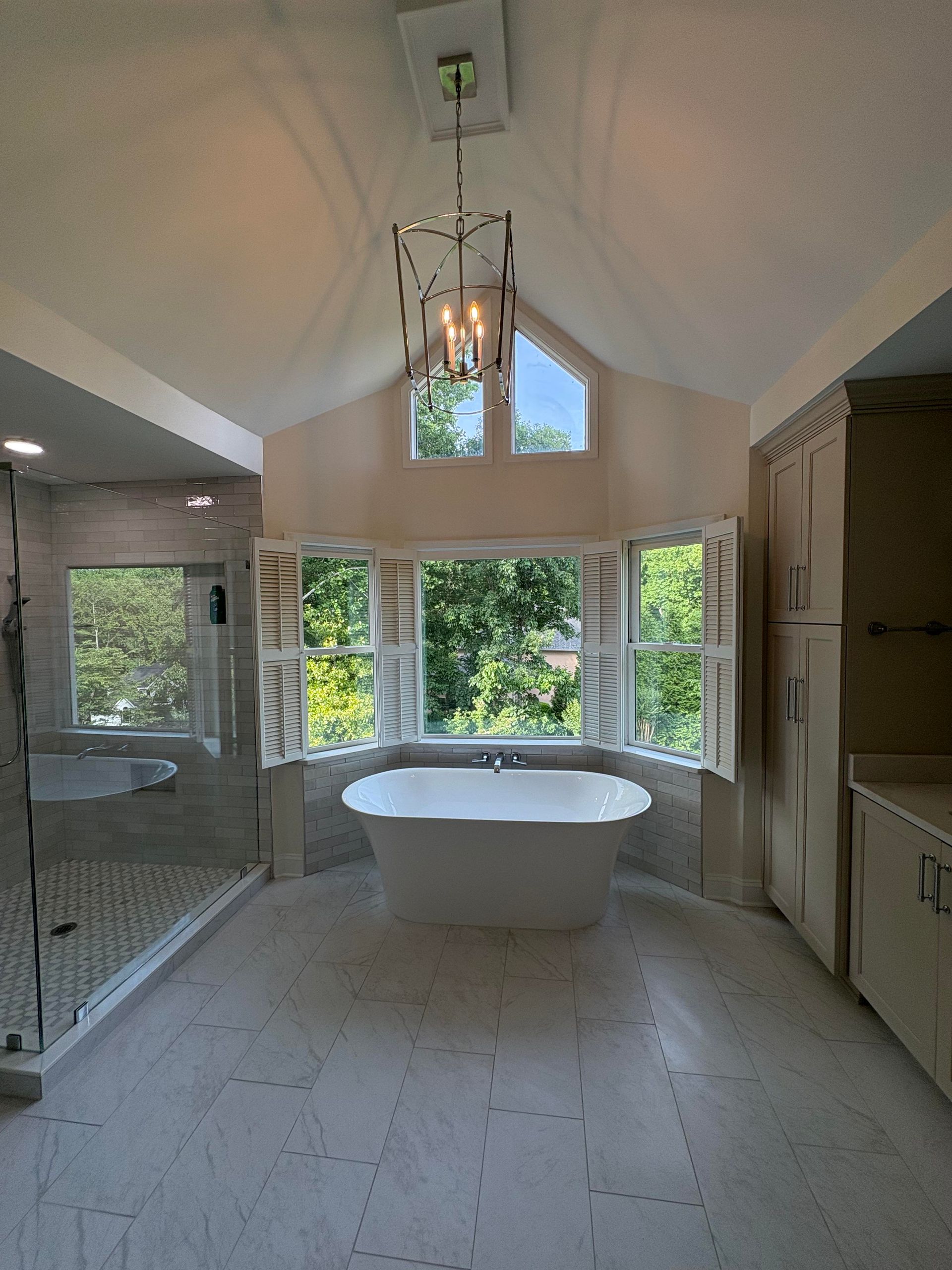 Spacious bathroom with a white freestanding tub, large windows, and elegant light fixture.