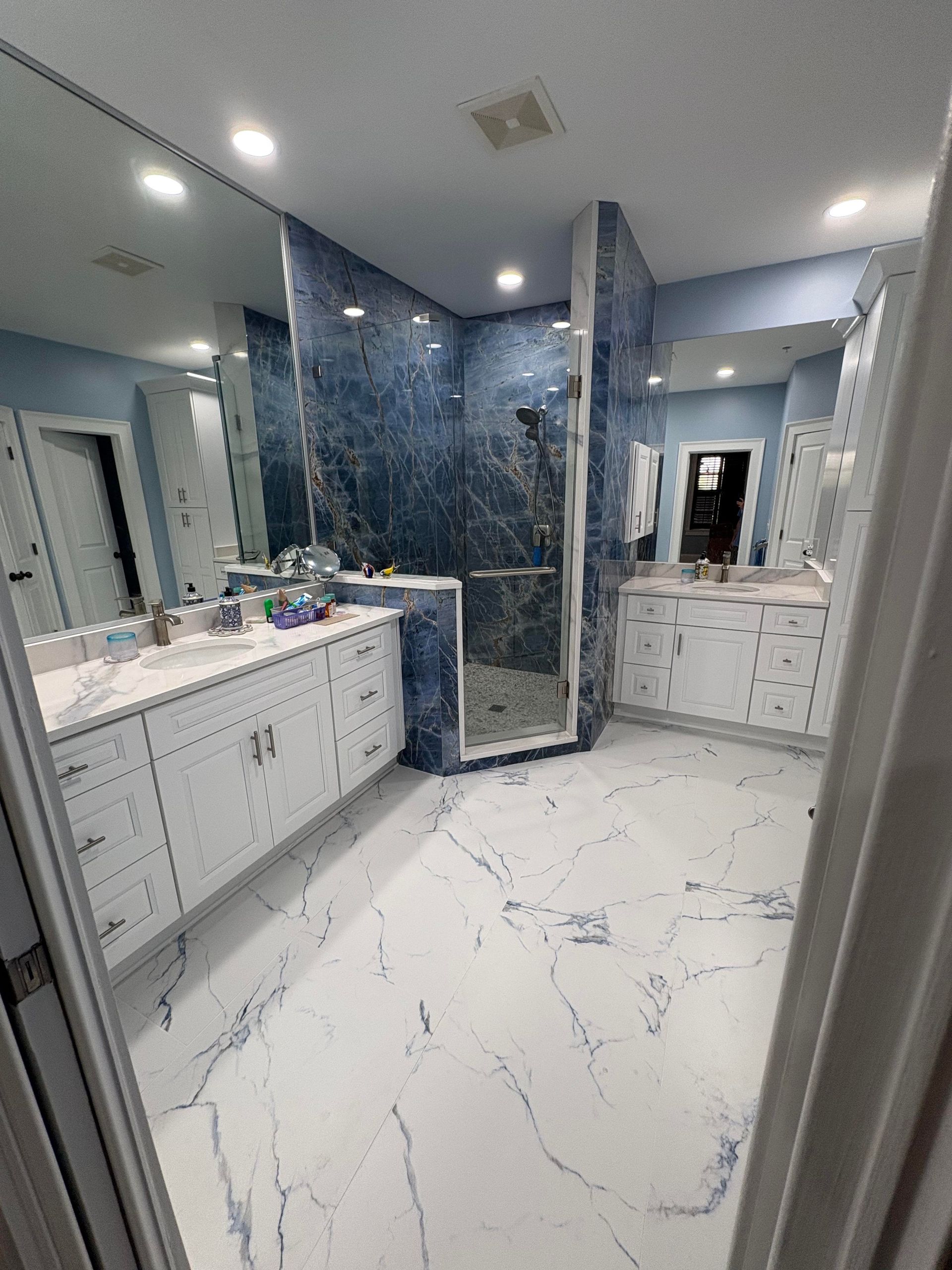 Spacious modern bathroom with blue tile shower, white vanities, and light blue walls.