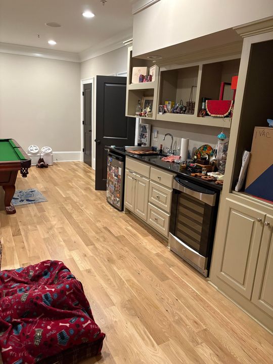 Long wooden floor, built-in cabinets, small kitchen area, pool table.