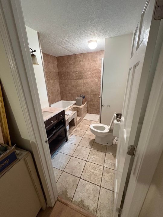 Bathroom interior with tile floor, bathtub, toilet, and brown tile wall.