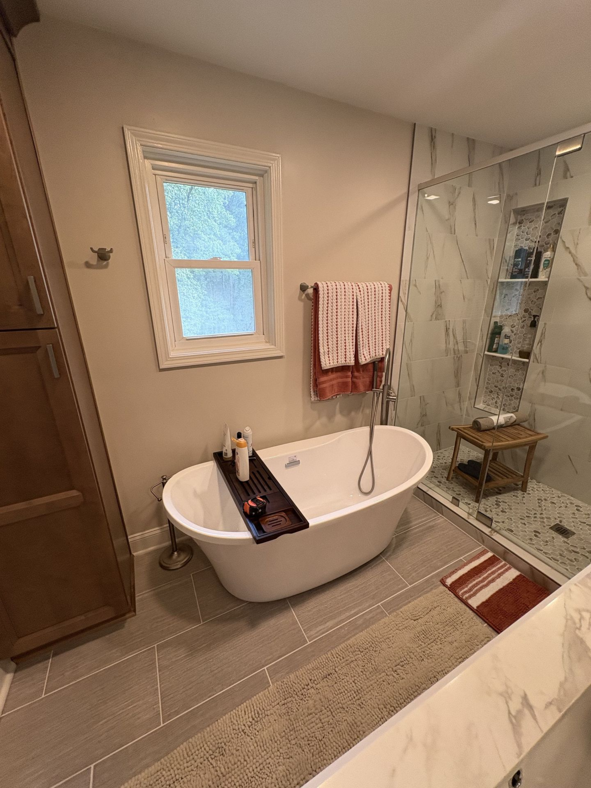 Bathroom with white oval tub, marble shower, and beige walls.