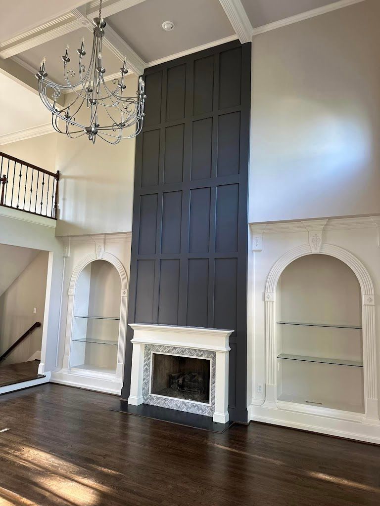 Spacious living room with fireplace, bookshelves, and dark gray accent wall. Elegant chandelier hangs above.