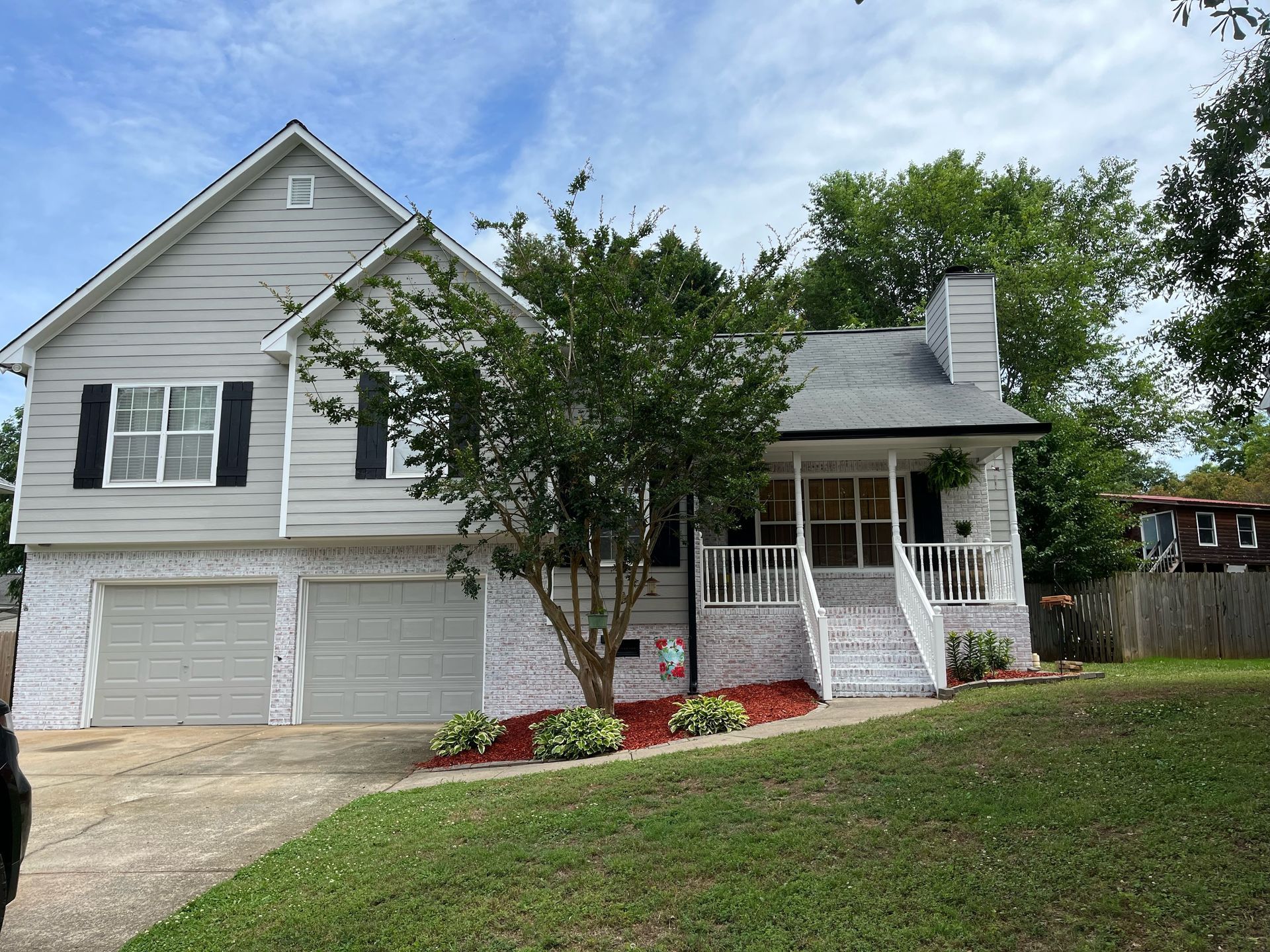 Two-story house with gray siding, attached garage, and a white-painted brick facade, front yard with green grass.