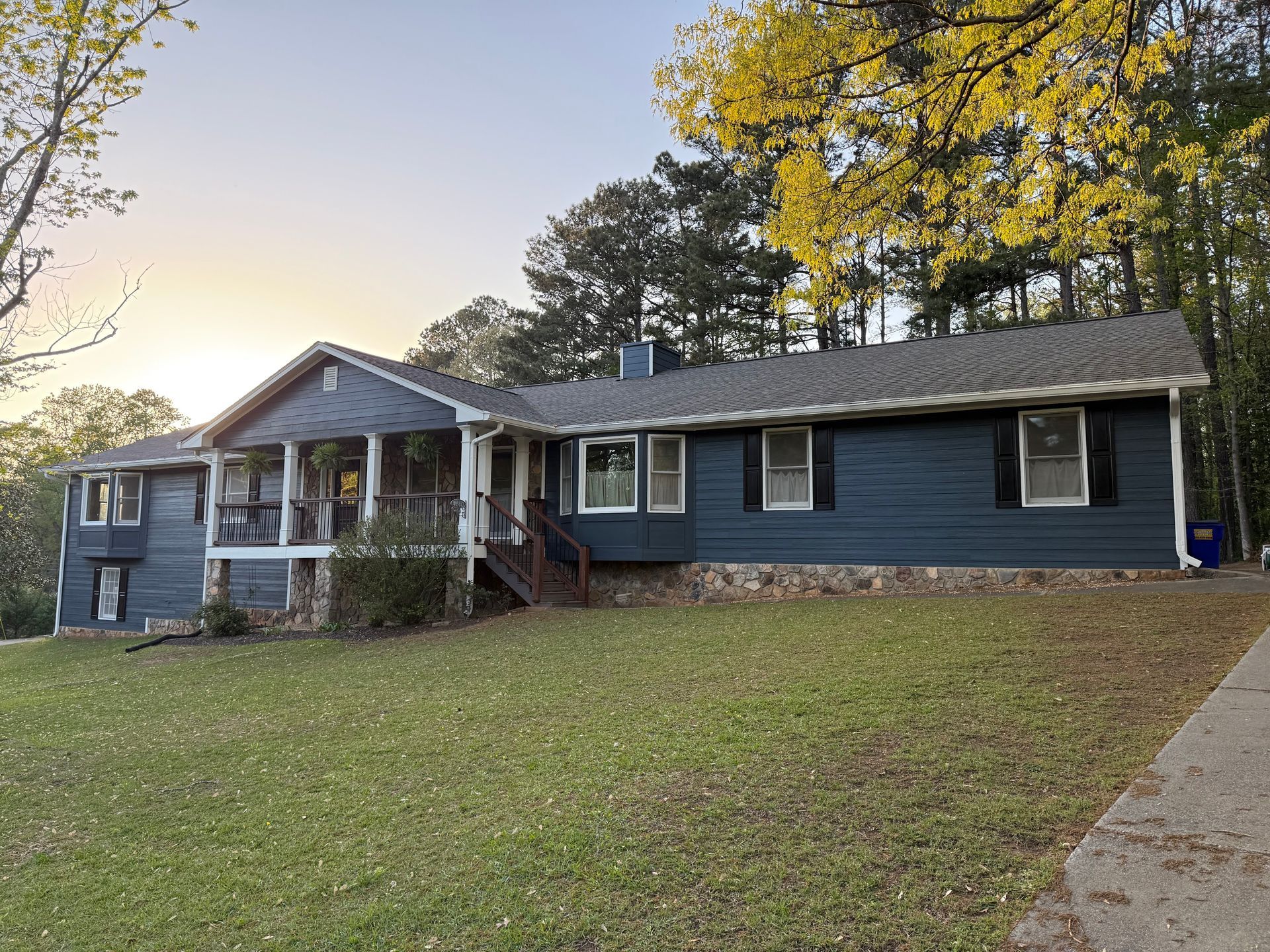 Blue house with porch and stone accents, set on a grassy hill with a driveway.