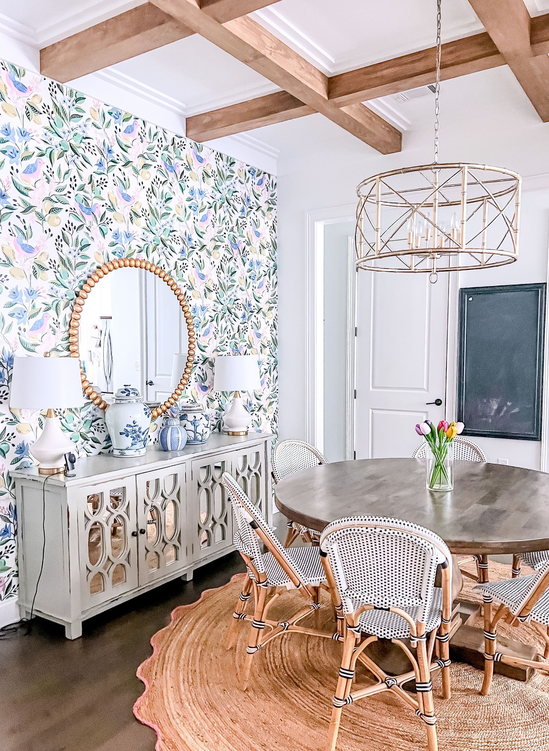 Dining room with floral wallpaper, a round table, and rattan chairs. Beige and blue color scheme.
