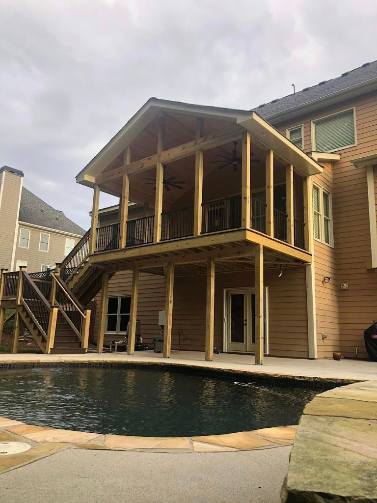 Two-story wooden deck with a covered roof, overlooking a dark pool. The deck is attached to a light brown house.
