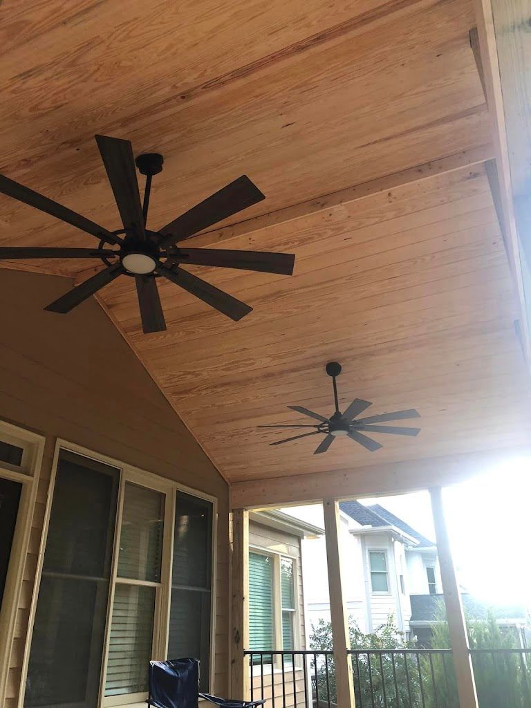 Two black ceiling fans hang from a light wood porch ceiling.