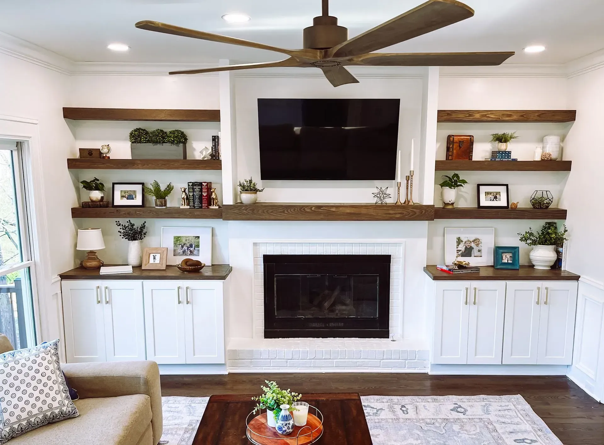 Living room with white built-in cabinets, fireplace, shelves with decorations, and a TV centered above the fireplace.