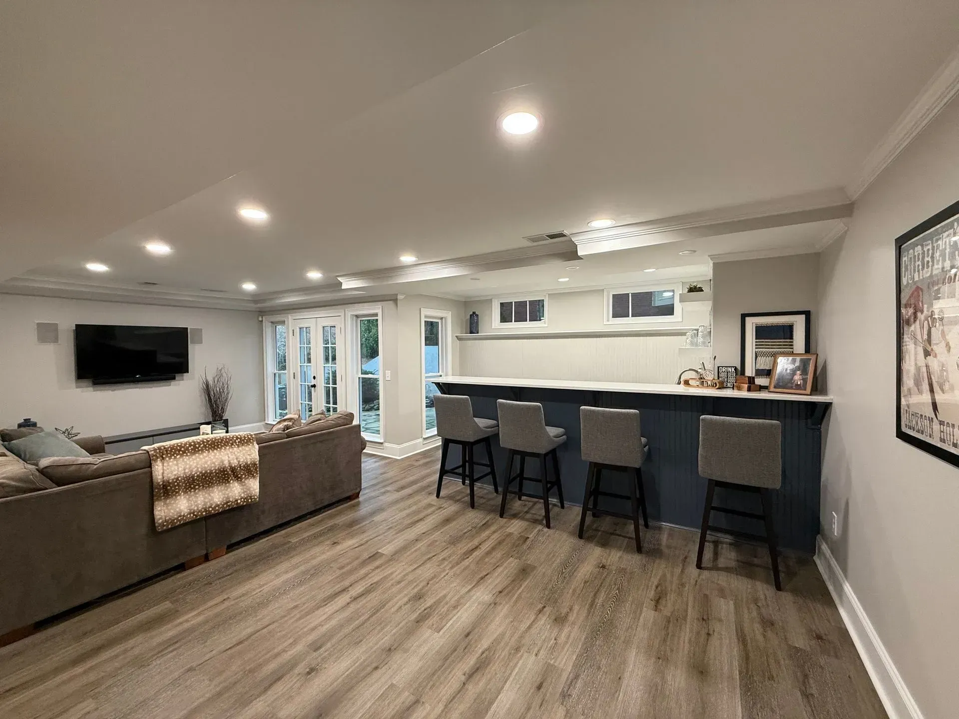 Basement with bar, seating, and a large sectional sofa. Gray and blue tones with wood flooring.