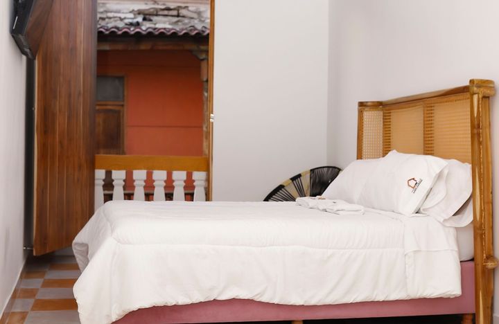 Dormitorio con cama, ropa de cama blanca, cabecero de mimbre y puerta que da a un balcón.