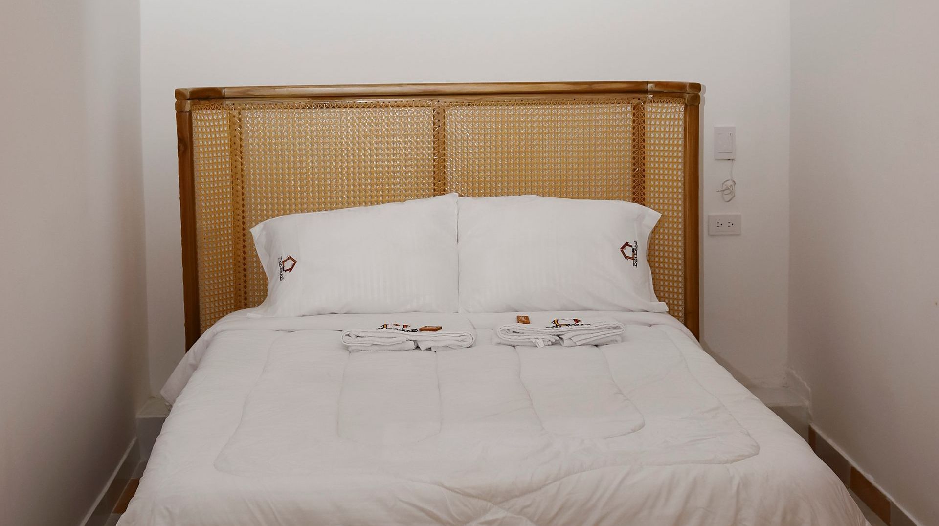 Bed with white linens, two pillows, and a woven headboard.
