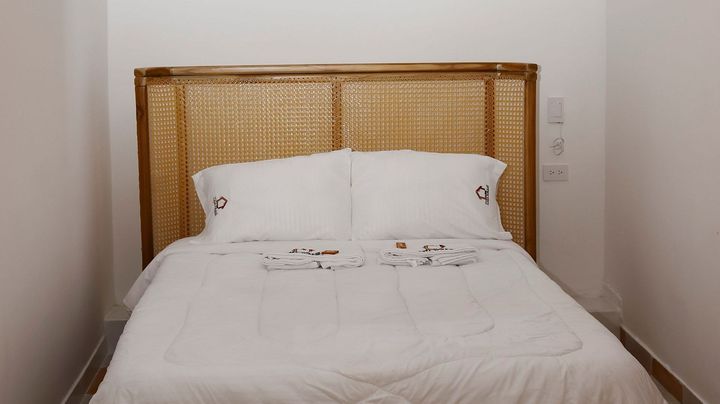 Una cama con cabecero de mimbre, sábanas blancas y toallas dobladas.