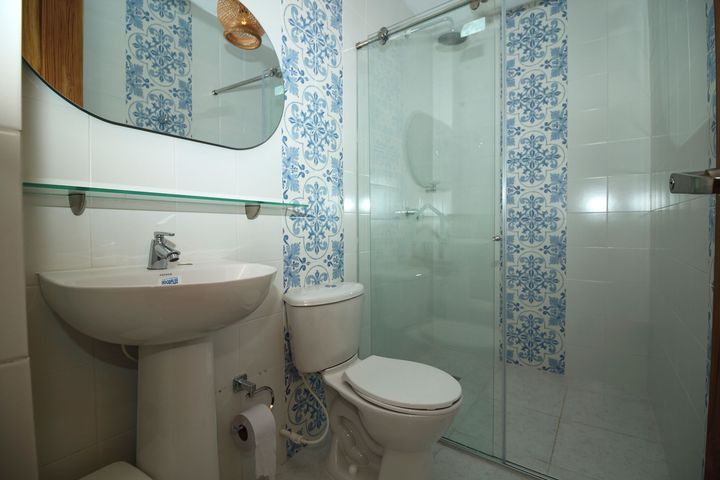 Baño con lavabo de pedestal blanco, inodoro, ducha de cristal y azulejos de pared con estampado azul.