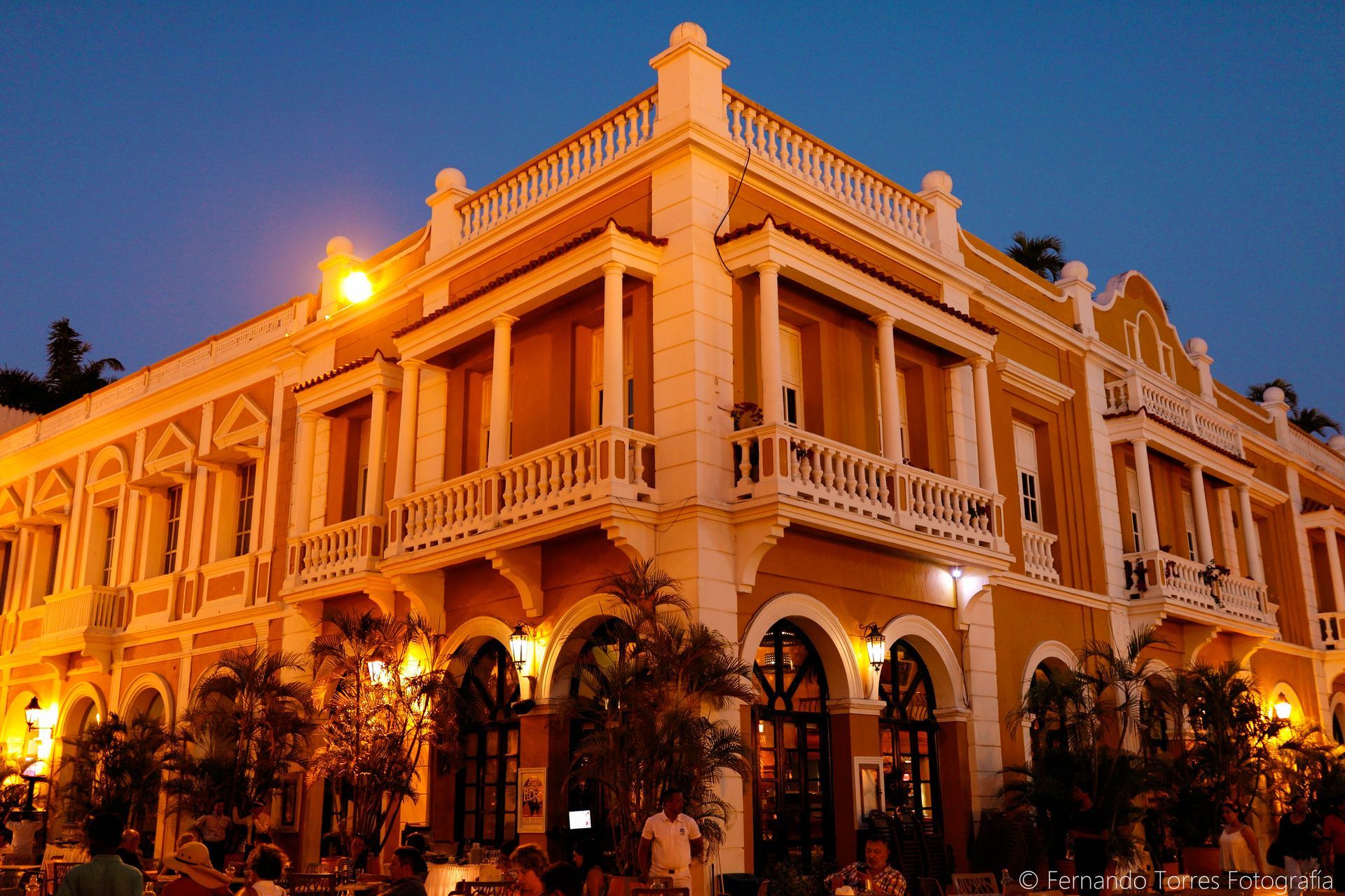 Edificio histórico amarillo con balcones e iluminación cálida al atardecer.