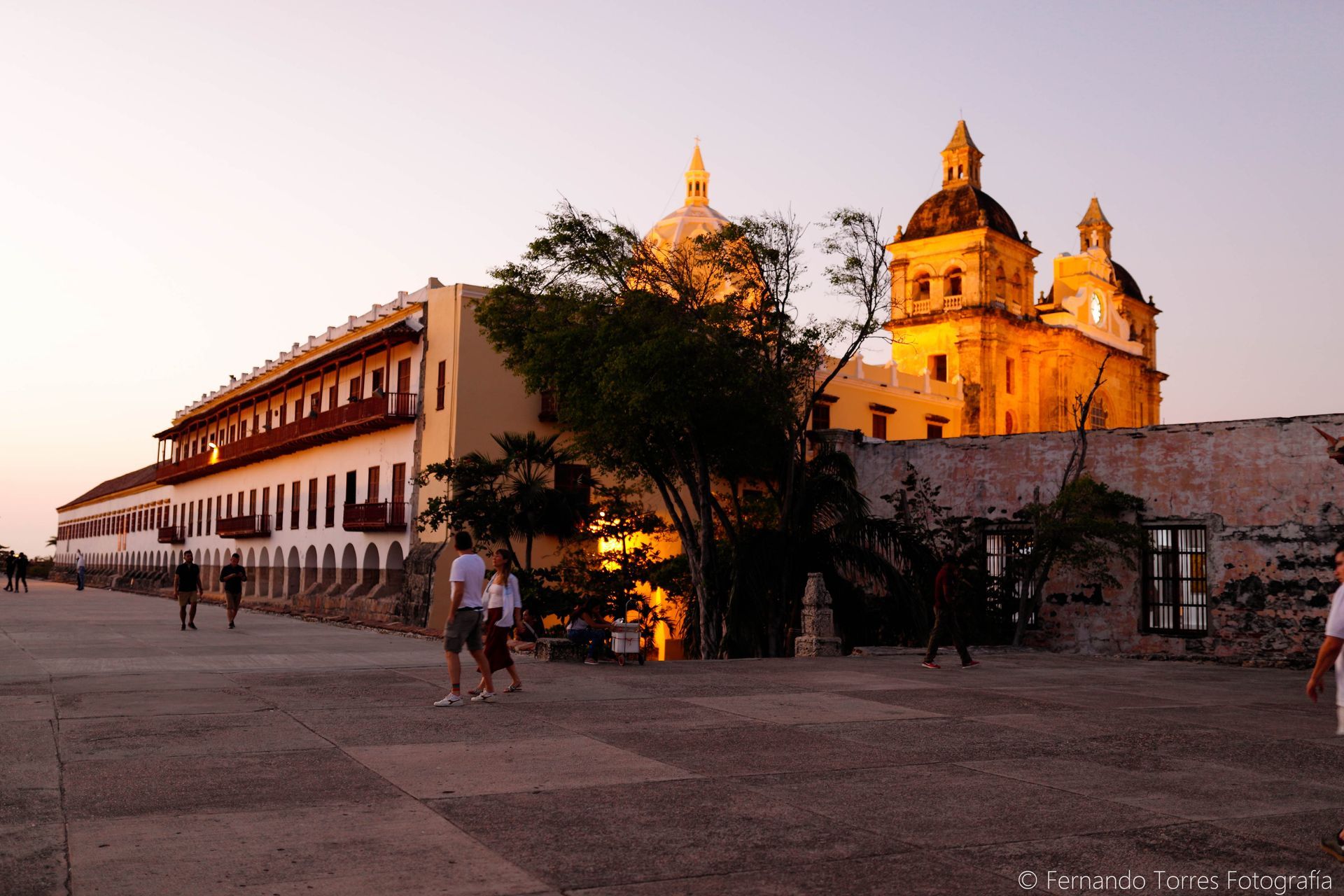 Edificios al atardecer en Cartagena, Colombia, con gente paseando por una plaza.