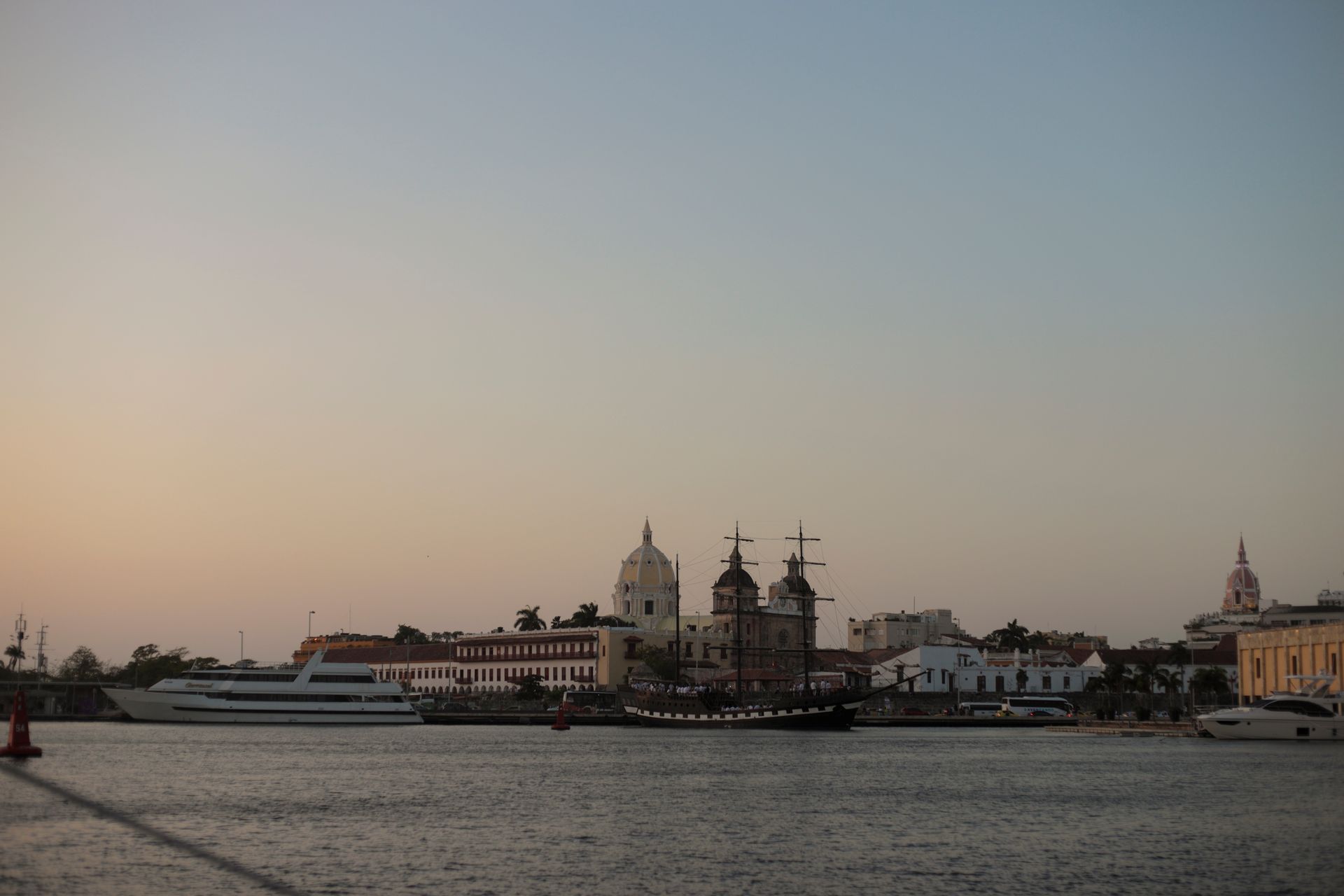 Paisaje urbano costero al atardecer con edificios históricos y barcos.