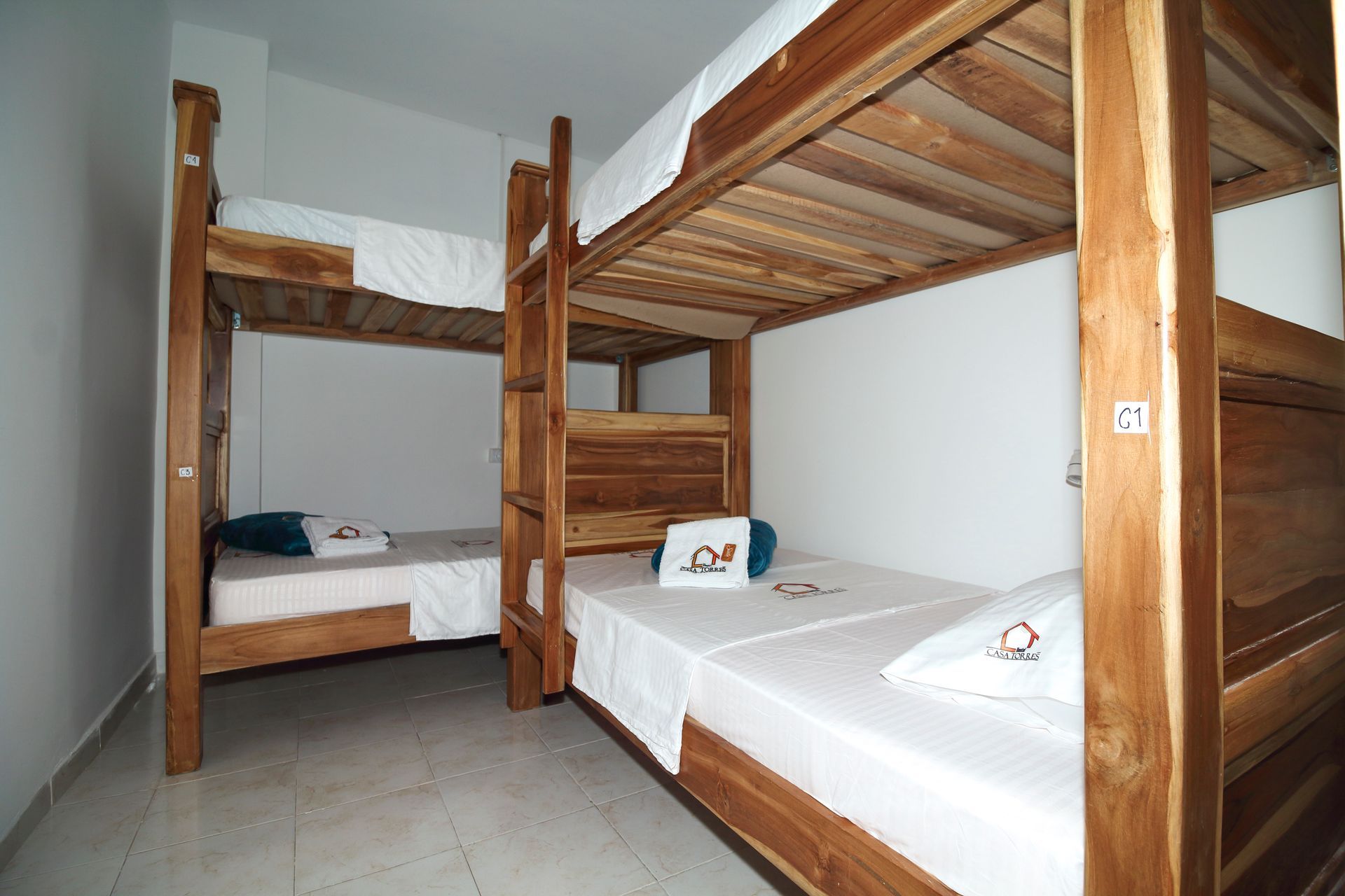 Dos literas de madera en una habitación de paredes blancas. Las camas están hechas con sábanas blancas.