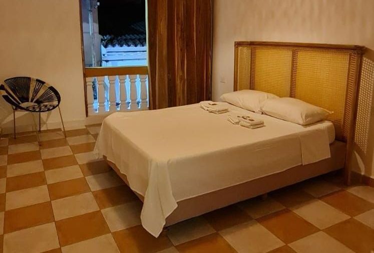 Dormitorio con cama doble, cabecero de mimbre, suelo ajedrezado y balcón.