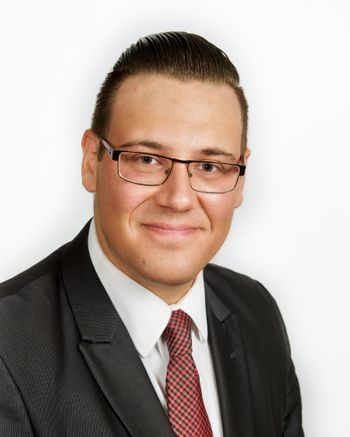Homme en costume et lunettes, souriant, avec une cravate rouge à motifs.