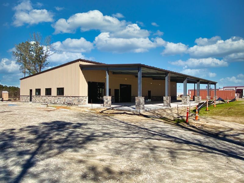 A large metal building with a covered porch is being built on a sunny day.