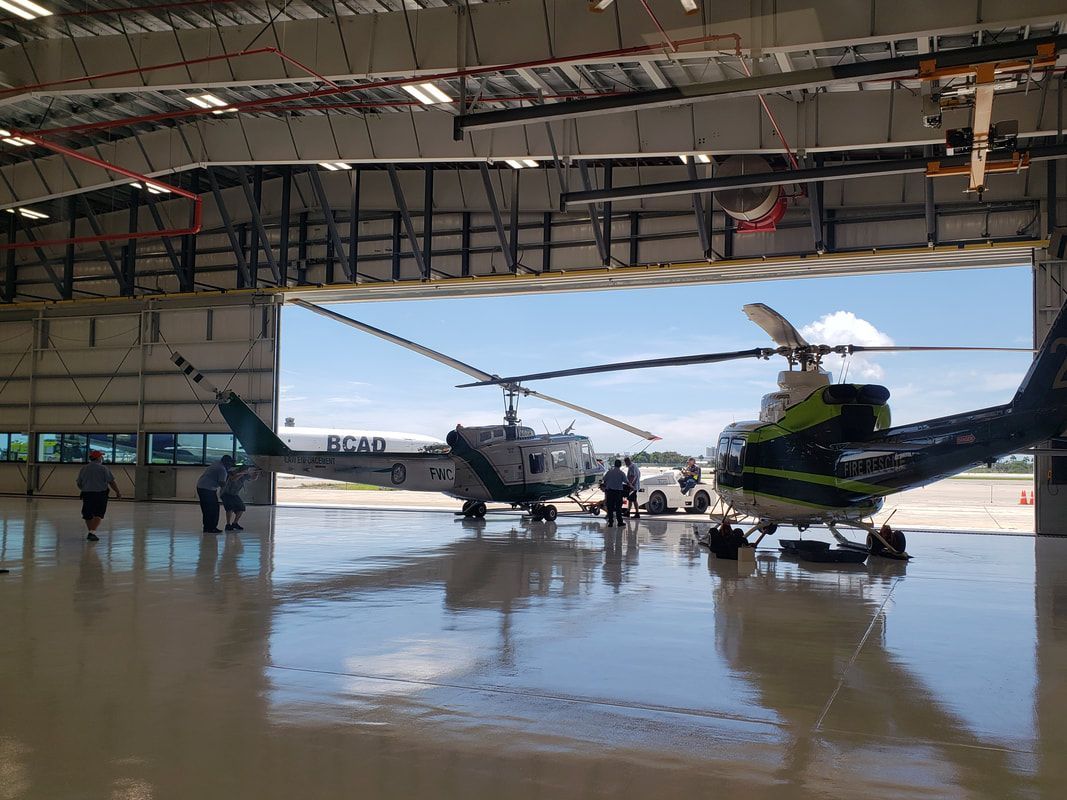 Two helicopters are parked in a hangar with the door open