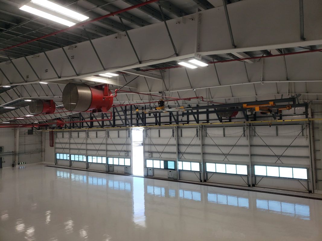 A large empty warehouse with a lot of windows and a crane hanging from the ceiling.
