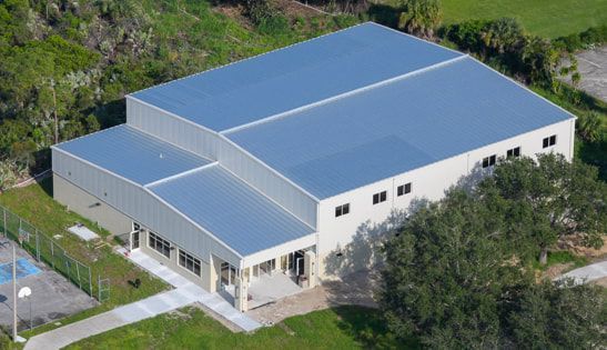 An aerial view of a large building with a metal roof surrounded by grass and trees.