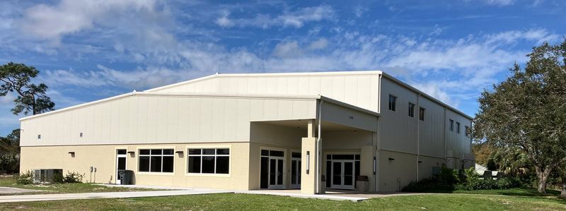 A large white building with a lot of windows is sitting on top of a lush green field.