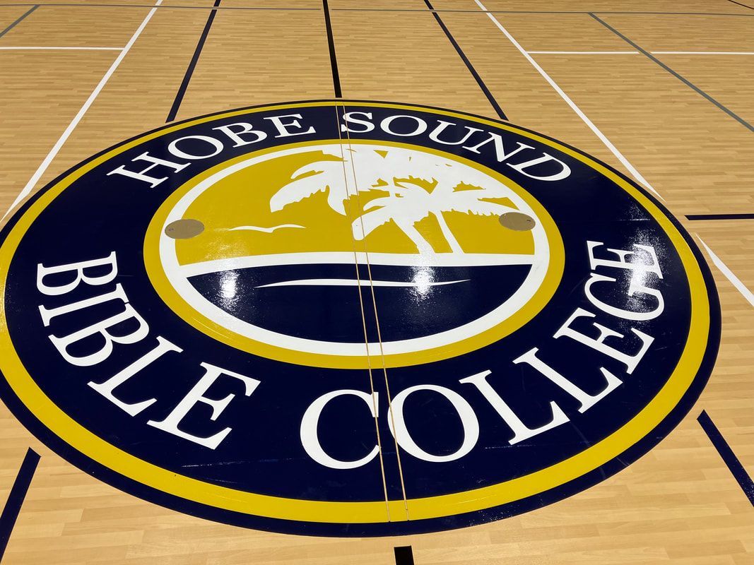 A logo for bible college is painted on the floor of a gym