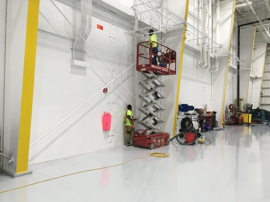 A man is standing on a scissor lift in a warehouse.