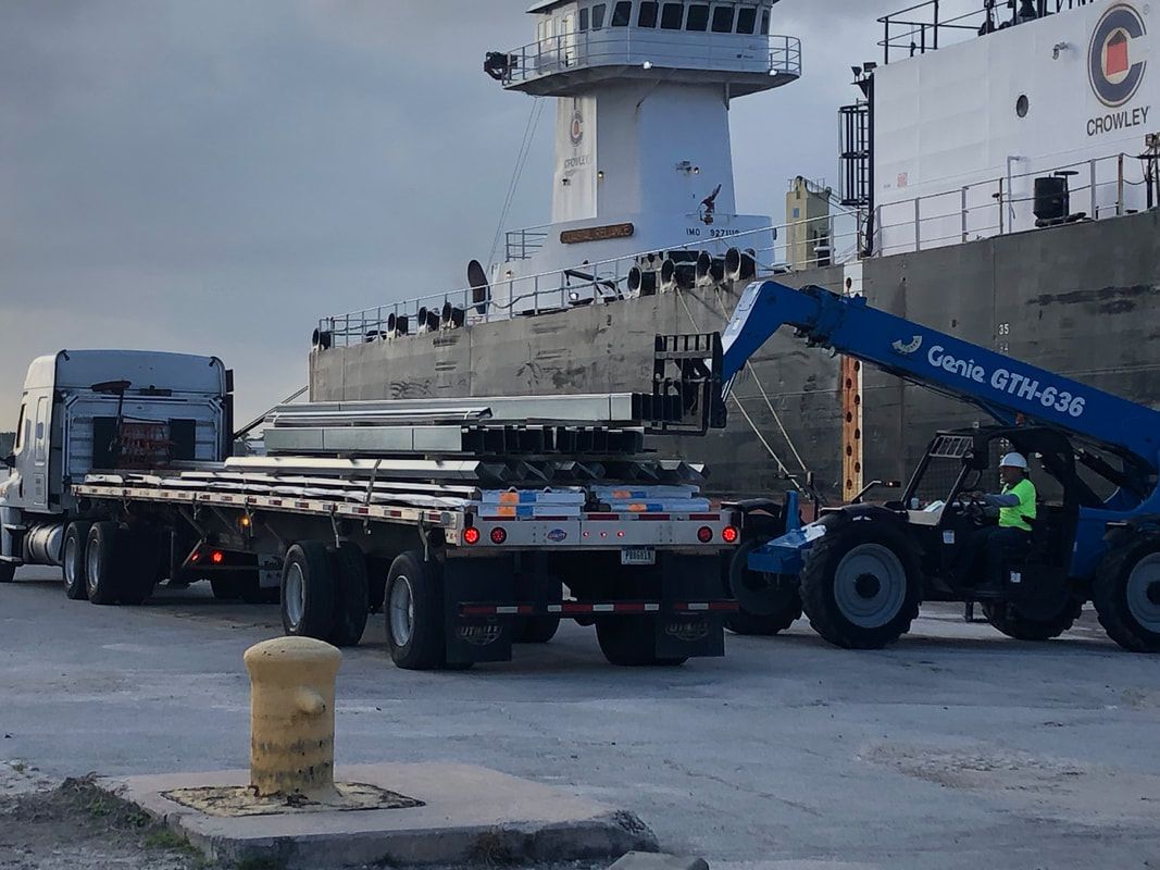 A truck is being towed by a forklift in front of a large ship.