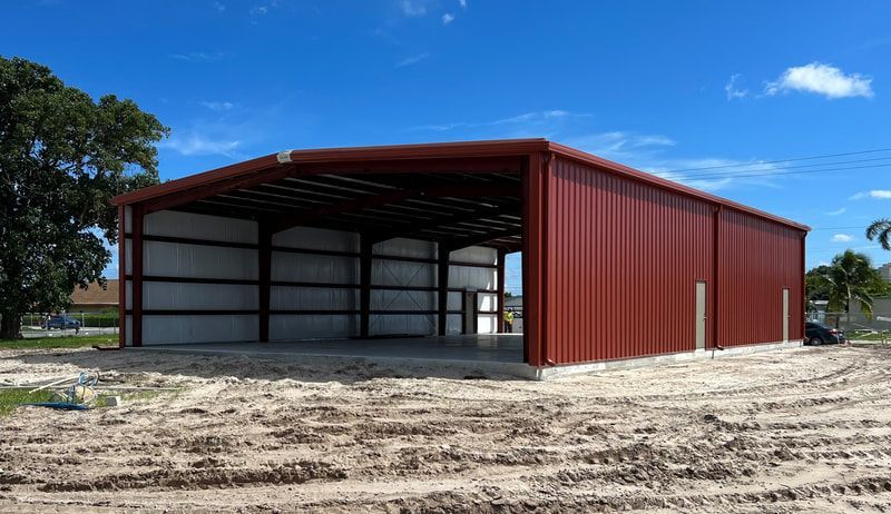 A large red metal building is sitting in the middle of a dirt field.