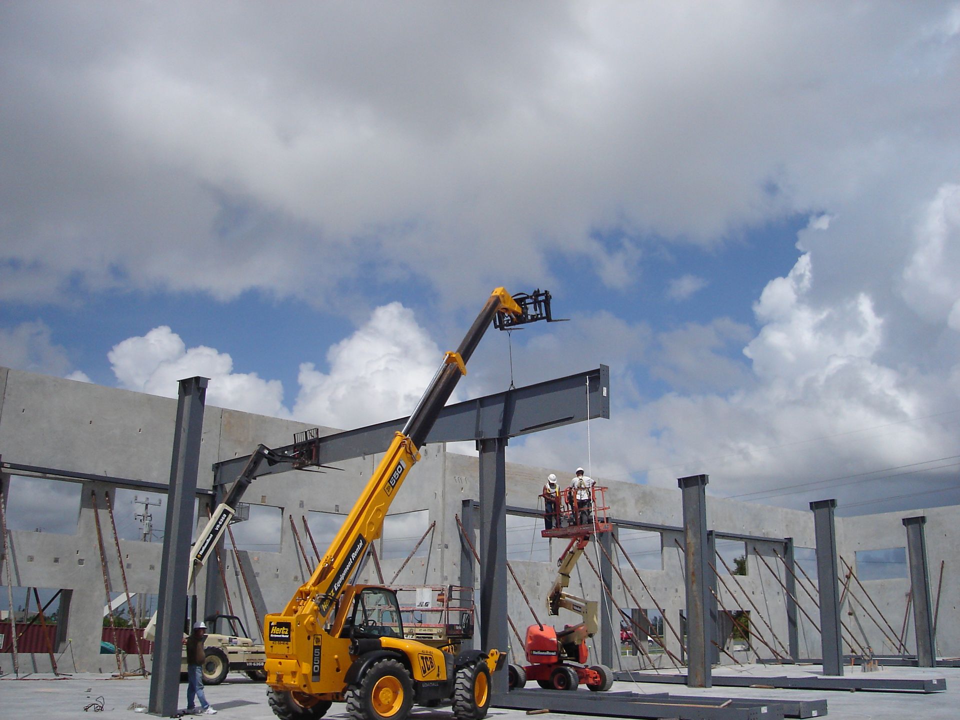 A construction site with a yellow crane lifting a metal beam
