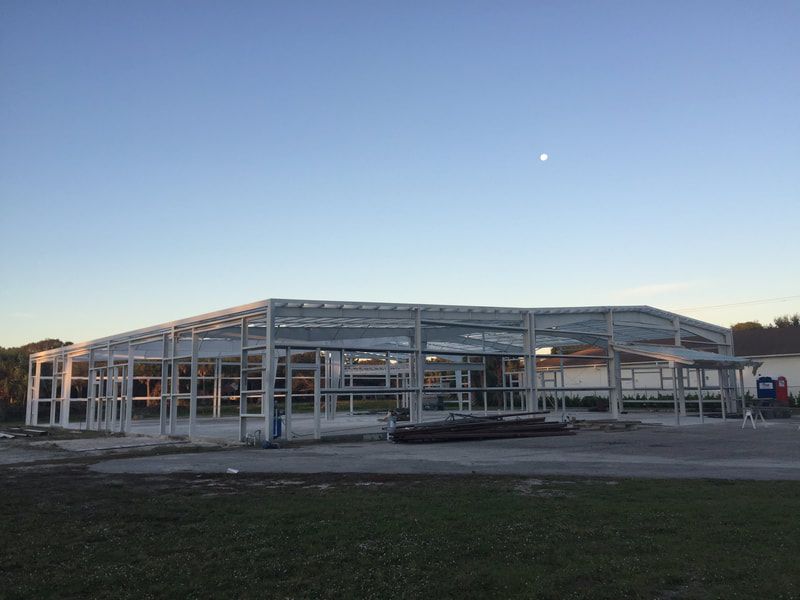 A large white building is being built in the middle of a field.