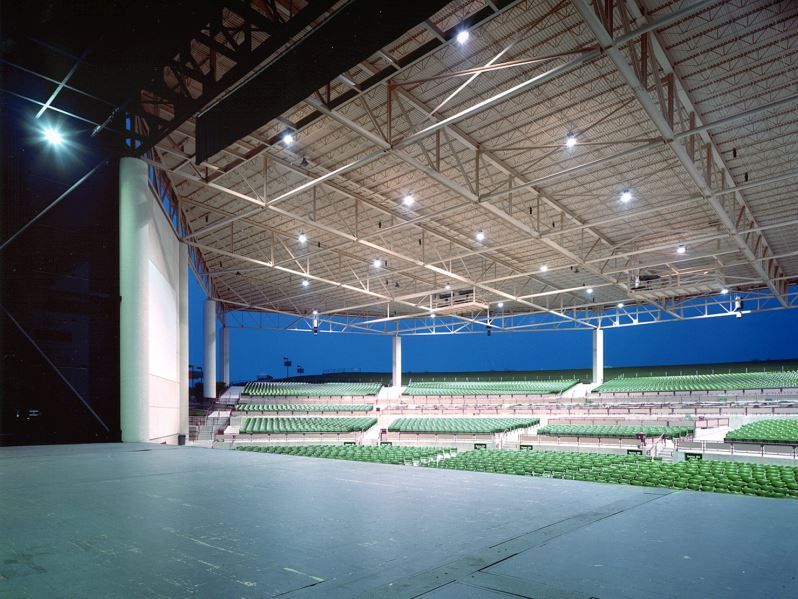 An empty stadium with green seats and a stage at night.