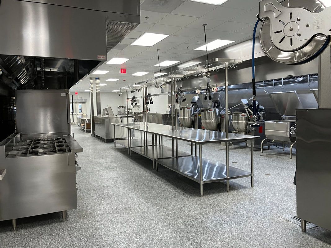 A large commercial kitchen with stainless steel appliances and a clock on the wall.