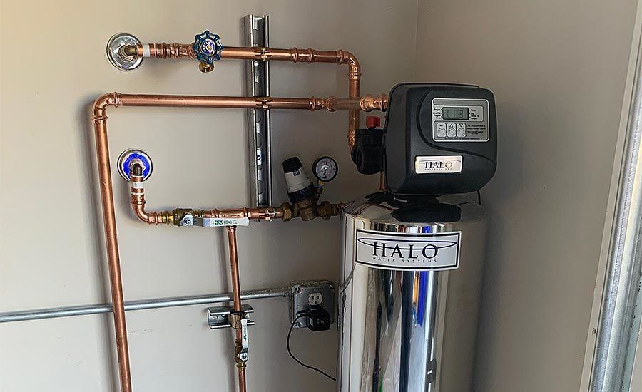 A water filter is sitting in a room next to copper pipes.